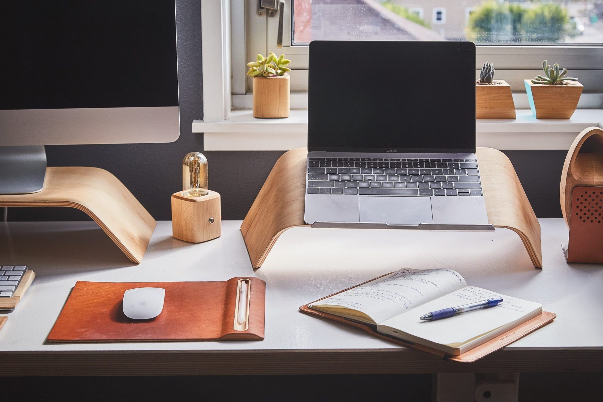 Mesa de home office com computador, óculos, café e cadernos.