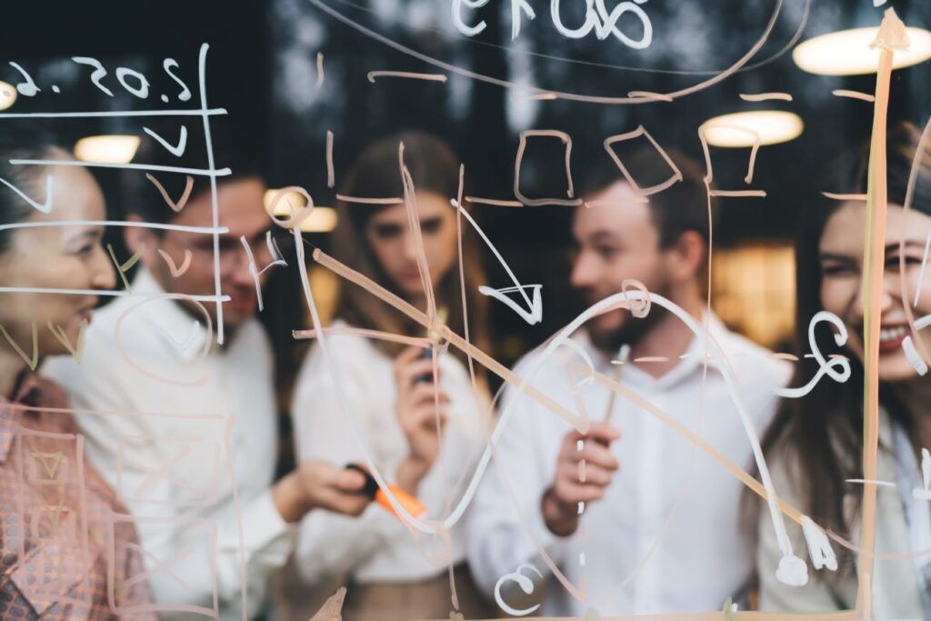 Grupo de pessoas escrevendo metas em uma lousa de vidro