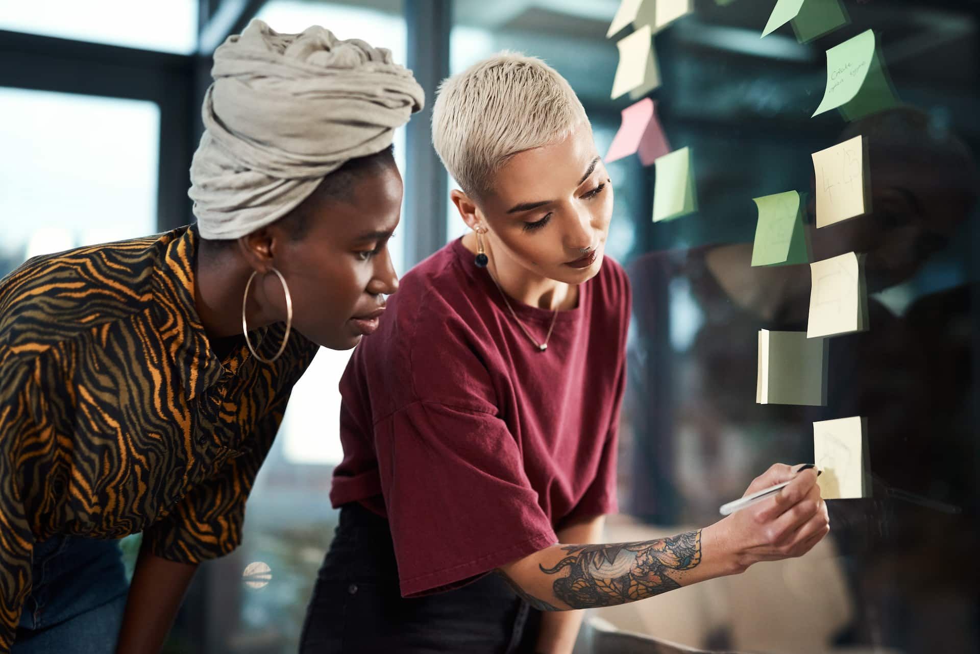 Duas mulheres conversando entrando escrevem em post its colados na parede.