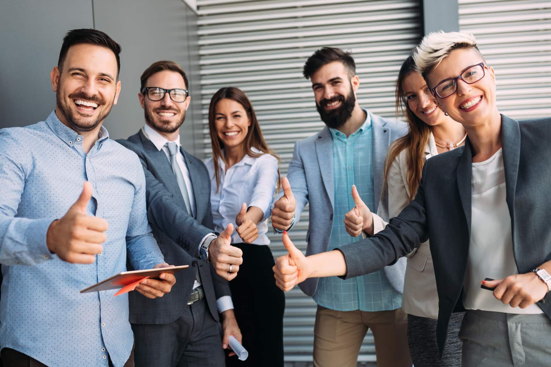 Grupo de pessoas sorrindo e fazendo "joia" com a mão. 