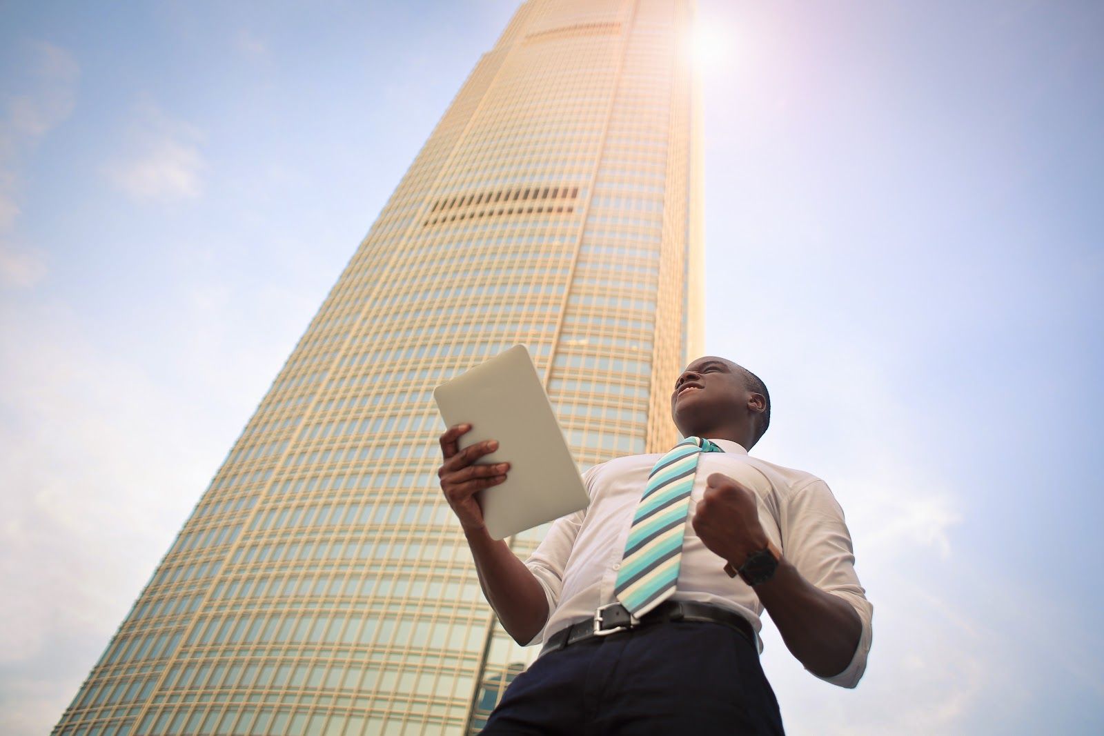 Um homem com um tablet na mão comemorando em frente de um prédio.