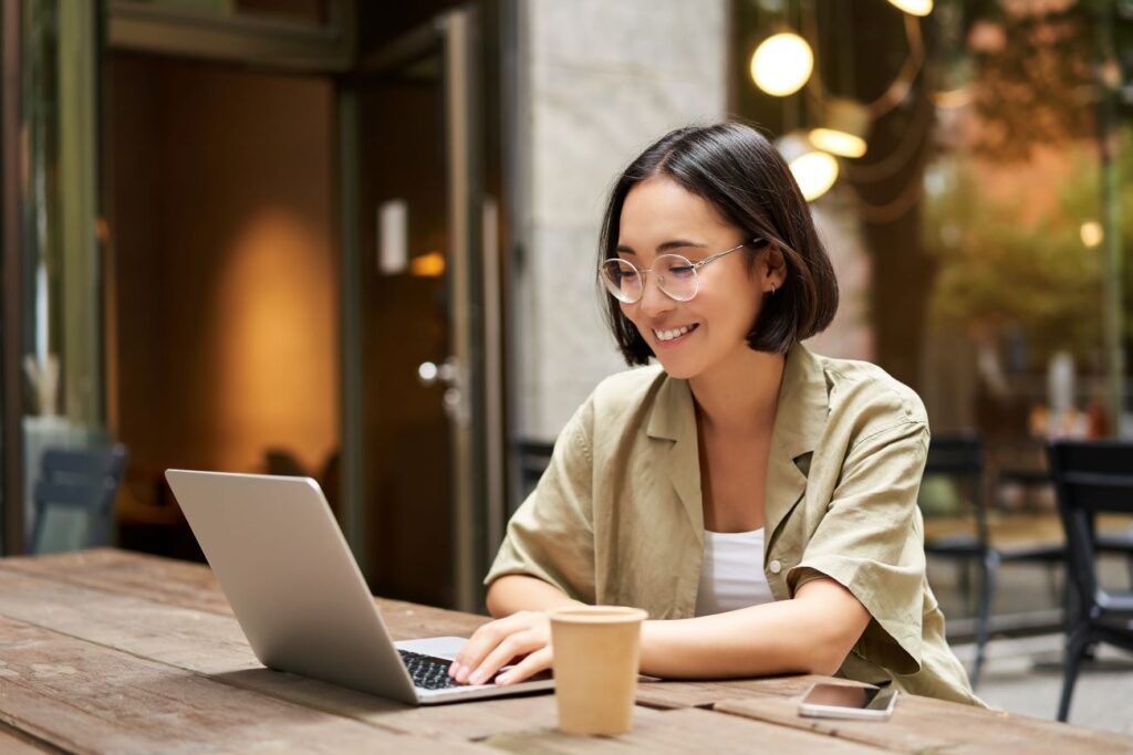Mulher jovem, sentada em uma cafeteria, trabalhando no notebook e bebendo um café.